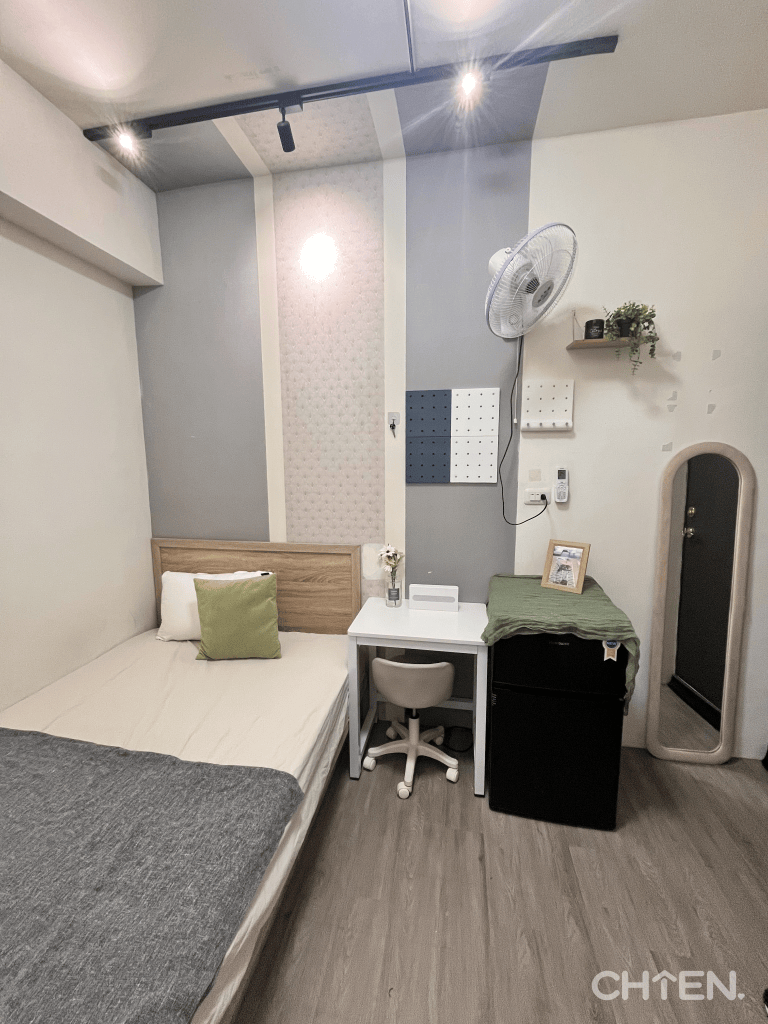 小套房布置全景，呈現床鋪、白色桌椅、冰箱、立鏡與壁面植栽